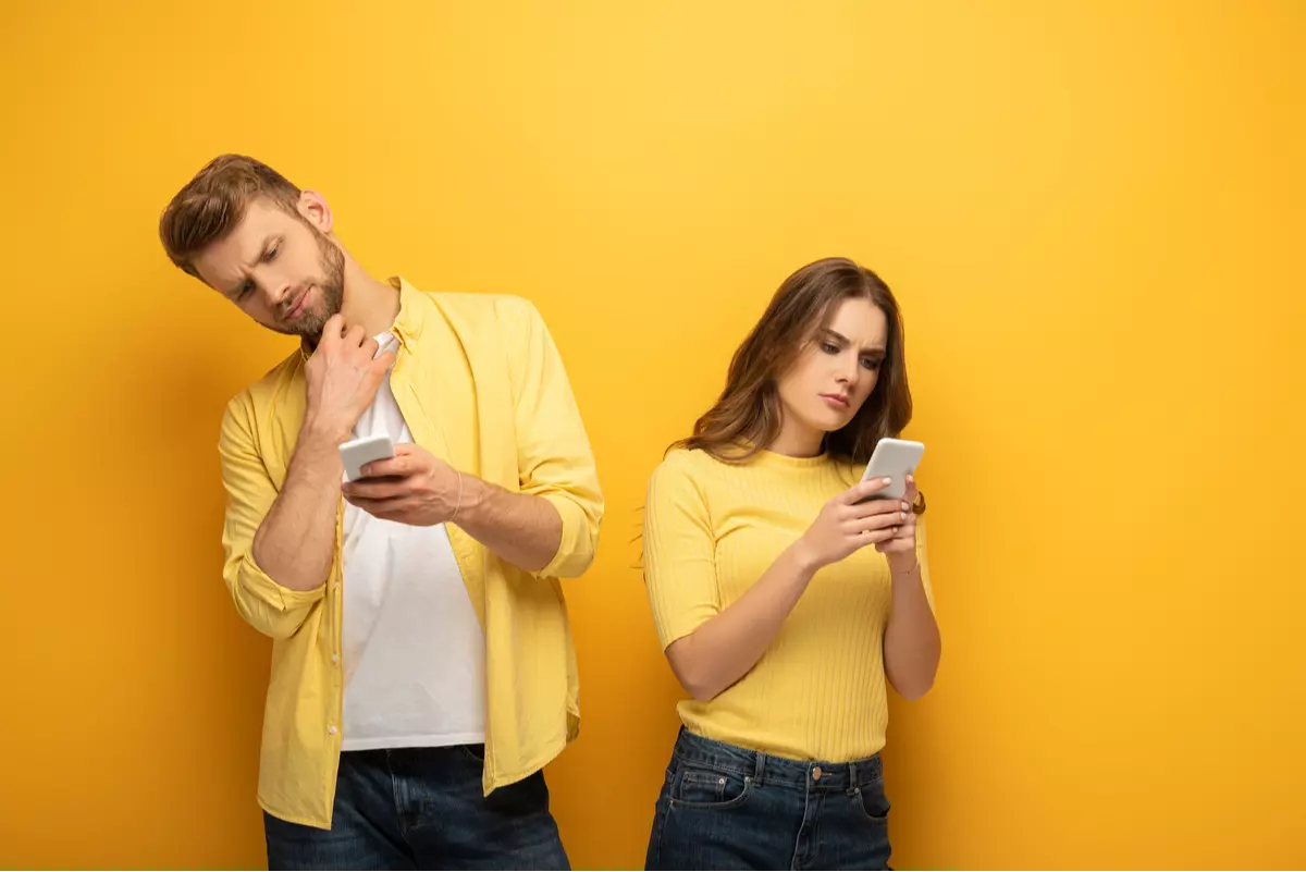 Man and woman looking at their phones while considering something.