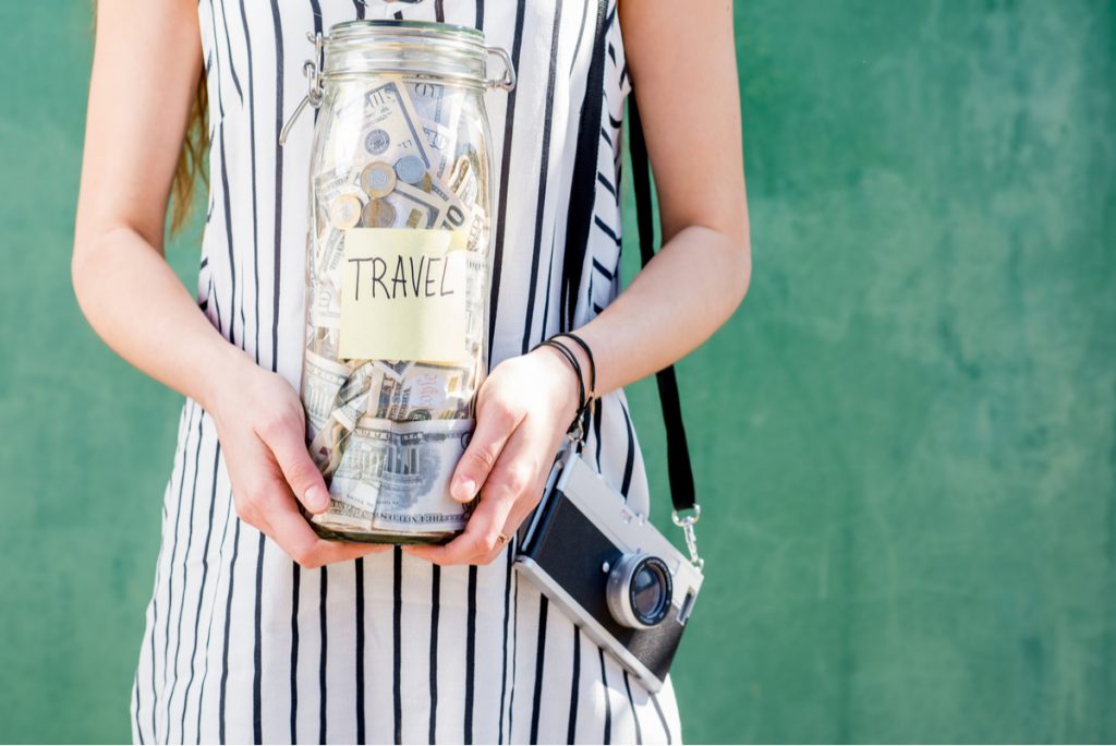 Woman holding a jar of money that is labeled for travel expenses.