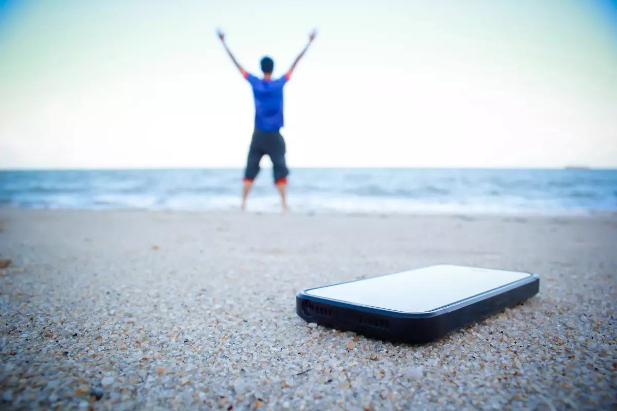 Man standing at the beach with his phone behind him.
