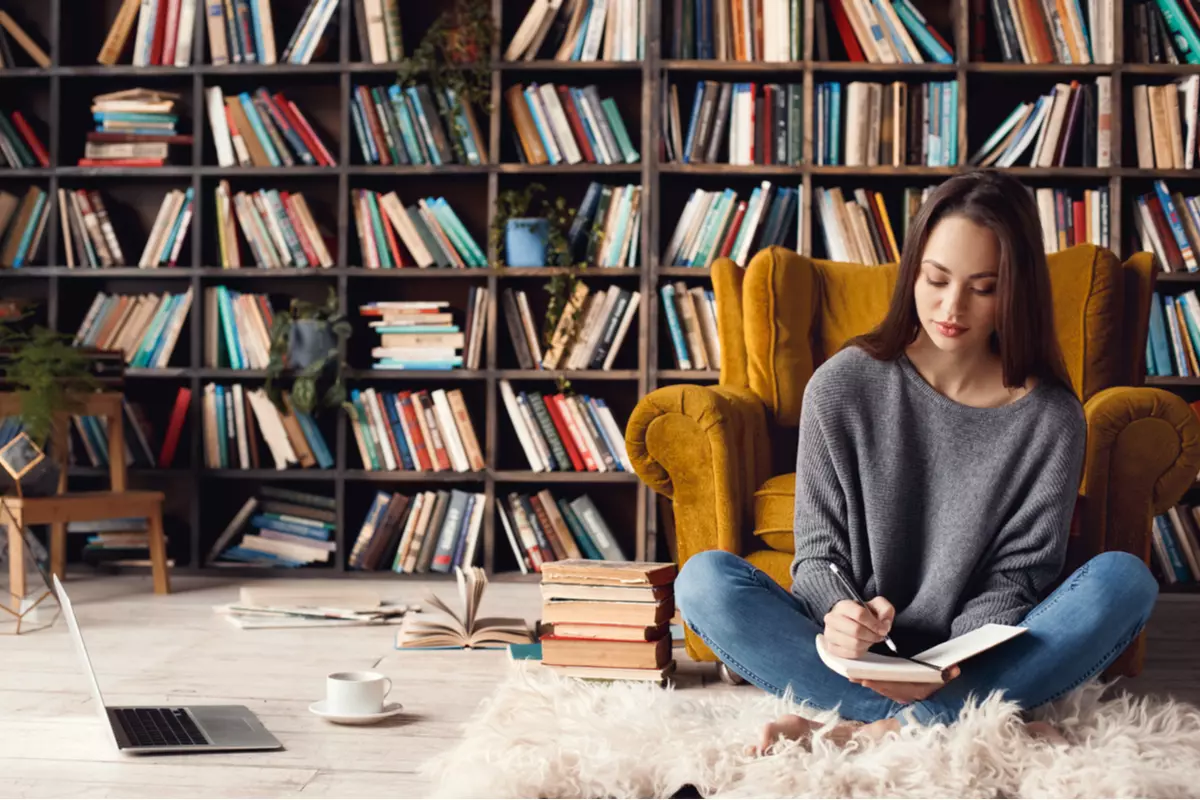 Woman writing in room with numerous books on shelves.