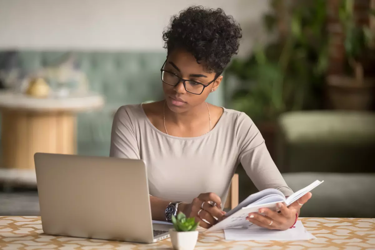 Woman researching stock market secrets on laptop with notebook