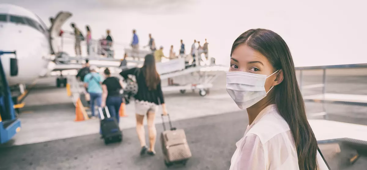 A woman boards an airplane wearing a facemask.
