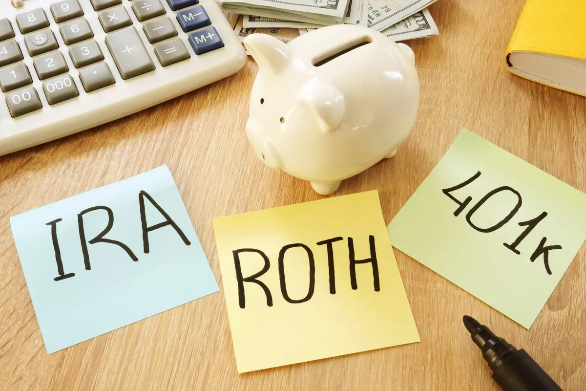 A piggy bank sits on a desk. Three post it notes on the desk read "IRA" "ROTH" and "401k."
