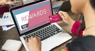 A woman holding a credit card and looking at her rewards on a laptop.