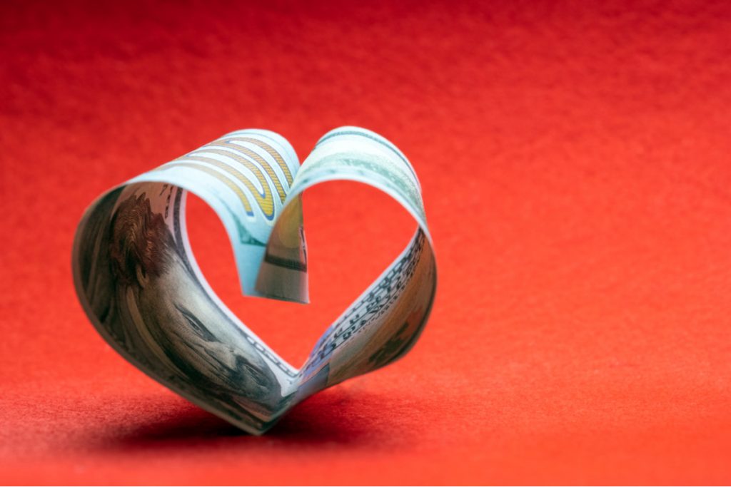 A hundred-dollar bill folded into a heart against a red background.
