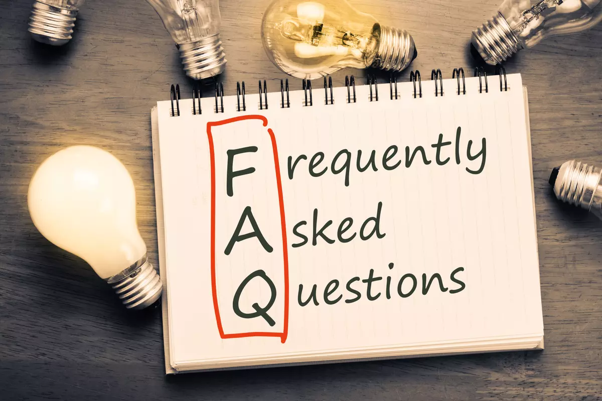 The text "Frequently Asked Questions" on a white notebook surrounded by lightbulbs. 