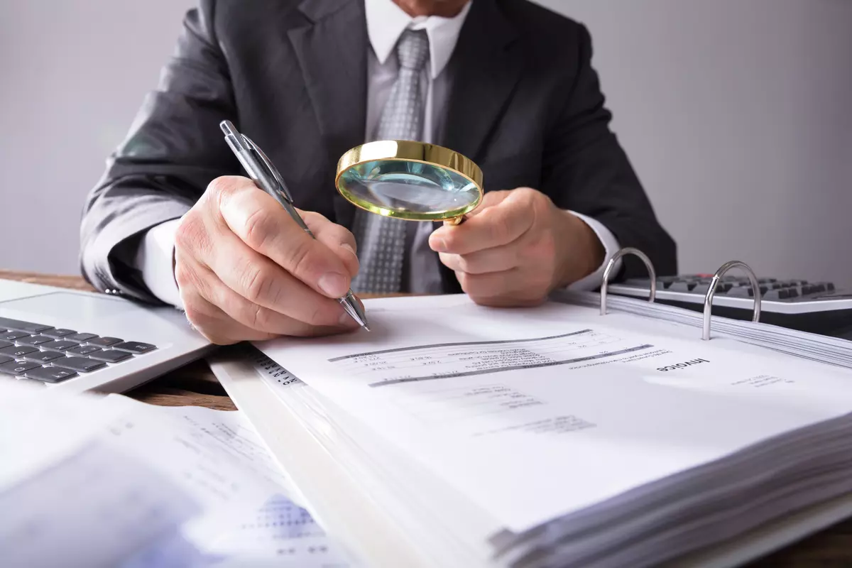 A businessman holding a microscope up to tax documents. 