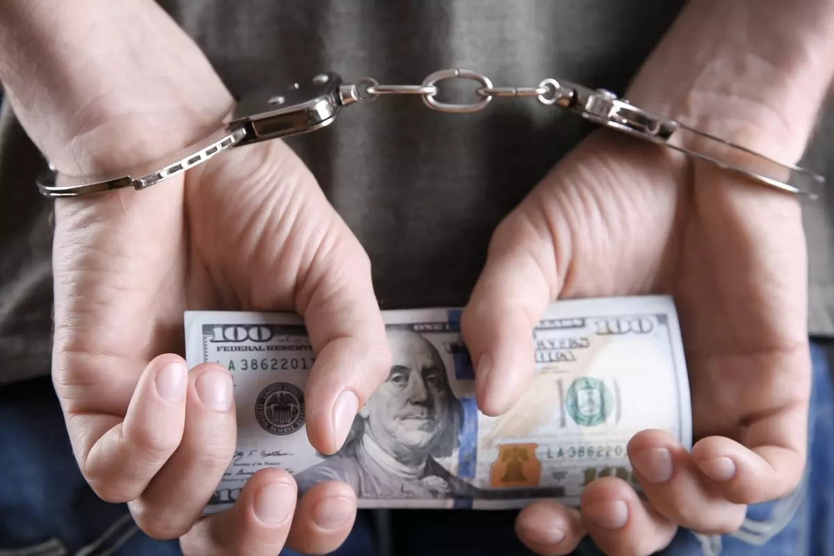 Man in handcuffs holding 100 dollar bills. 