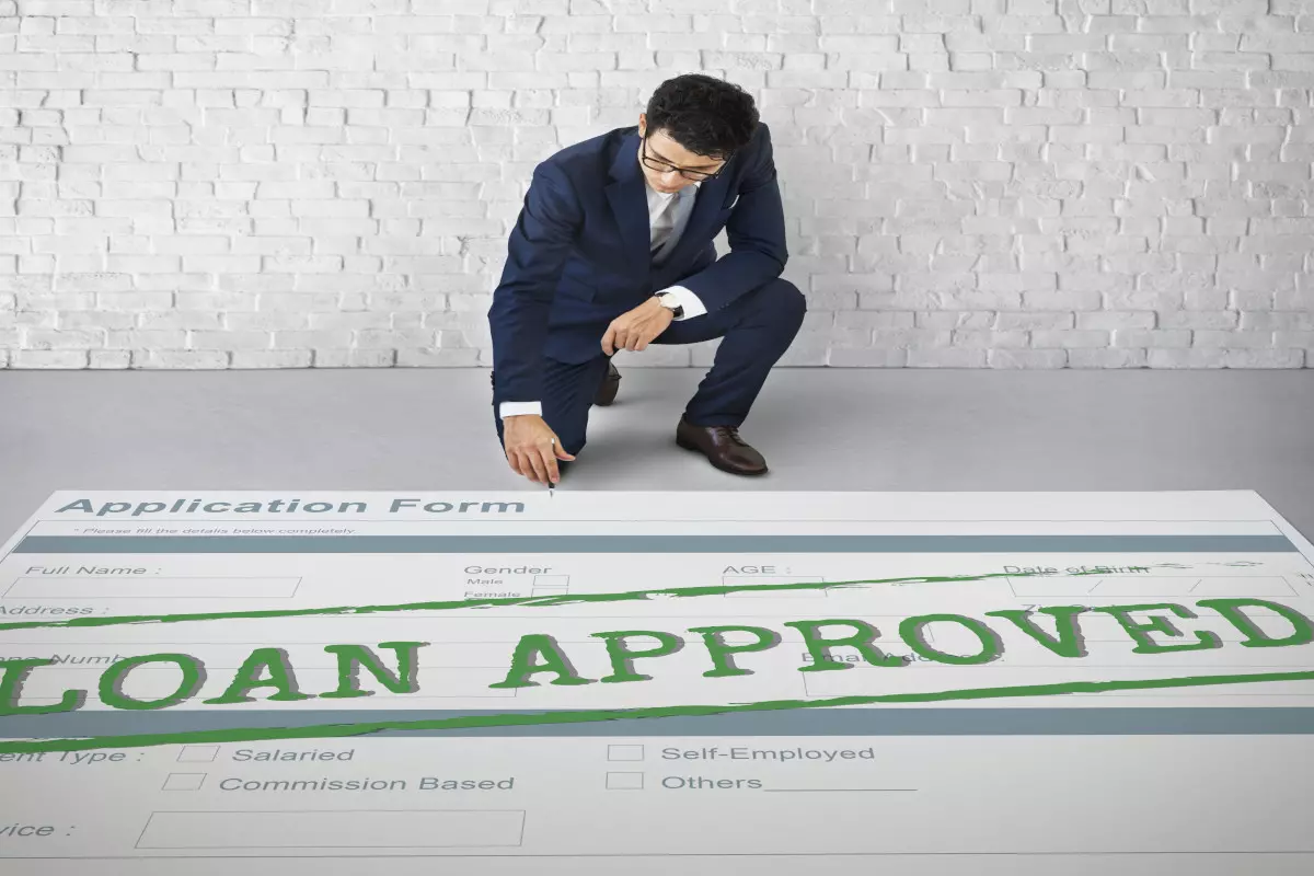A loan officer staring down at an oversized application form with the words "loan approved" stamped across it. 