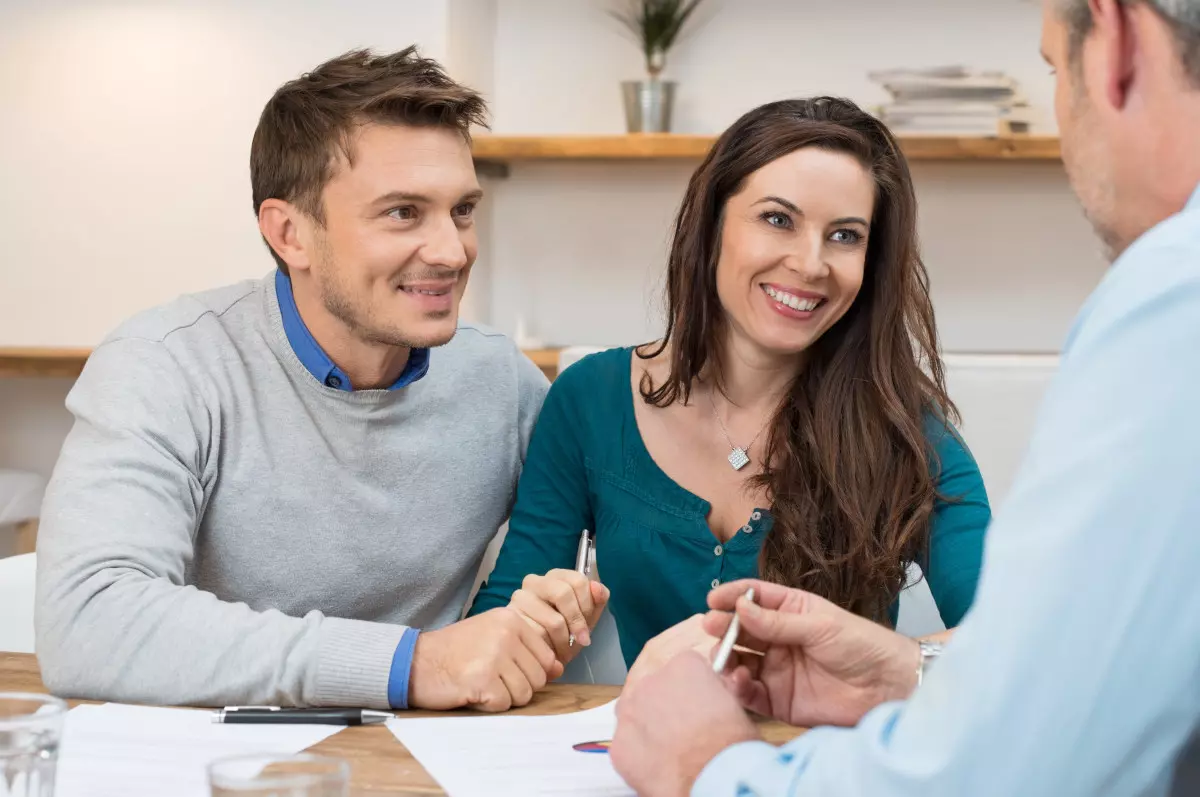 A couple smiling and signing a loan contract. 