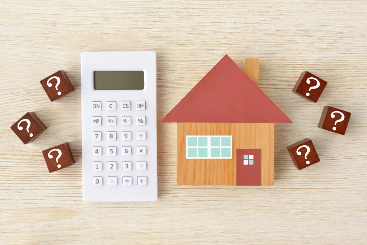 A calculator next to a wooden block house and question marks. 