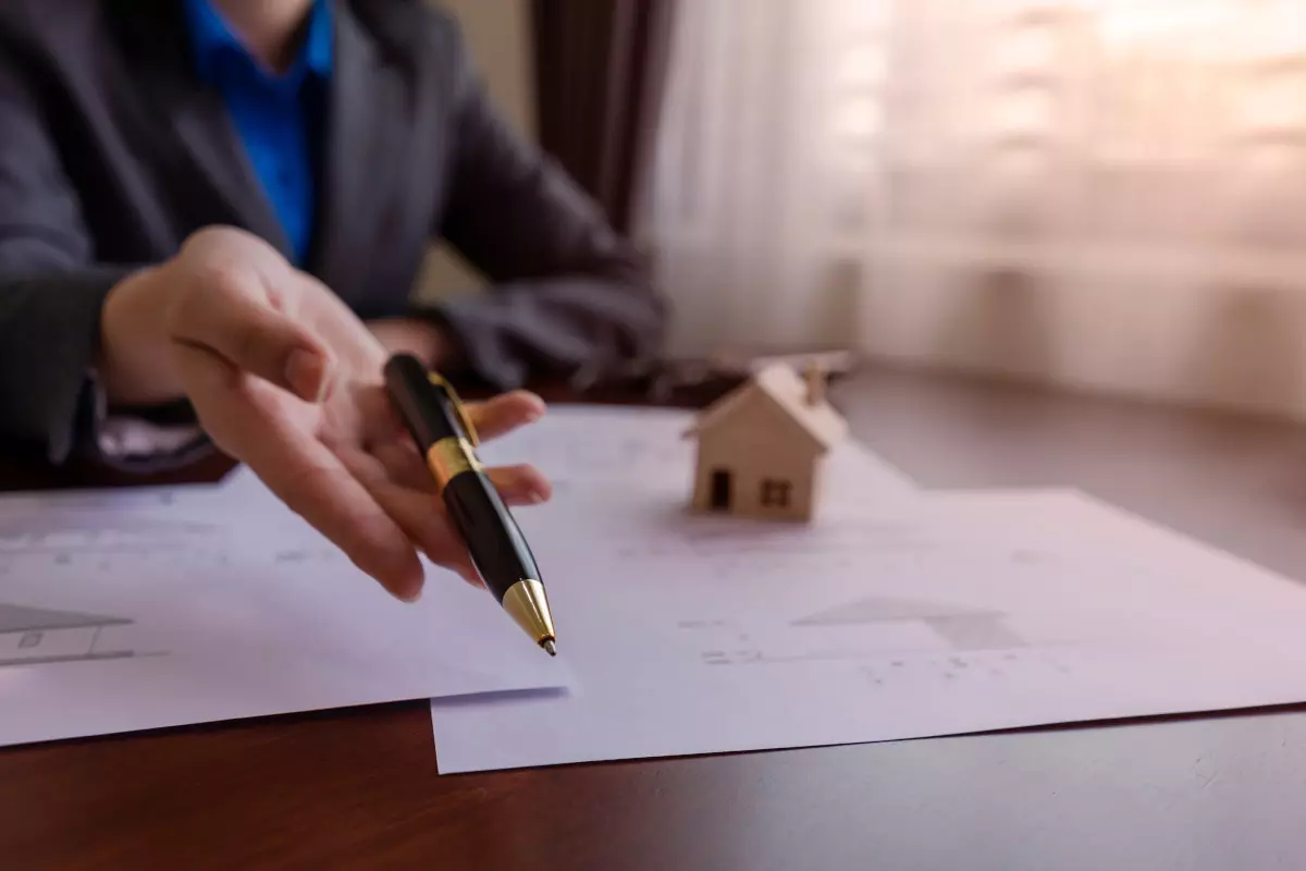 A loan officer holding out a pen for the client to sign a loan contract. 