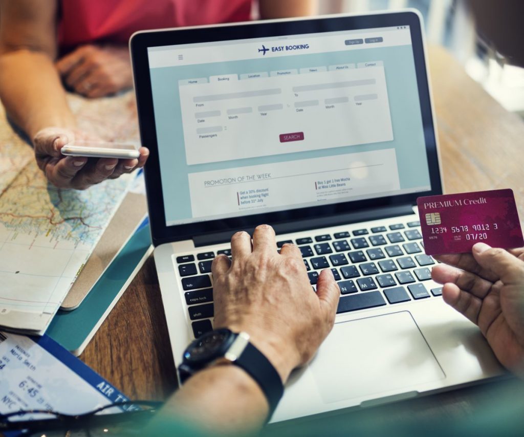 Individual holding credit card and booking flight on laptop.