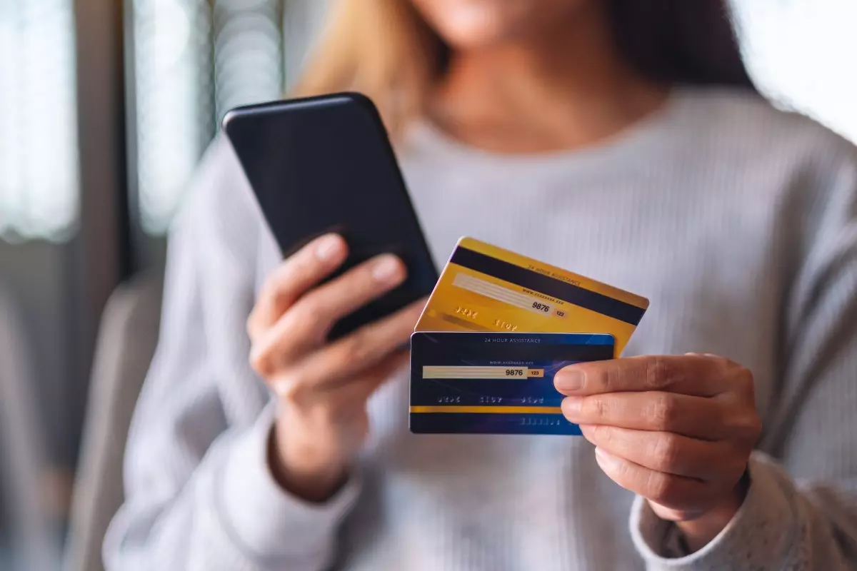 Young adult holding cellphone and two credit cards.