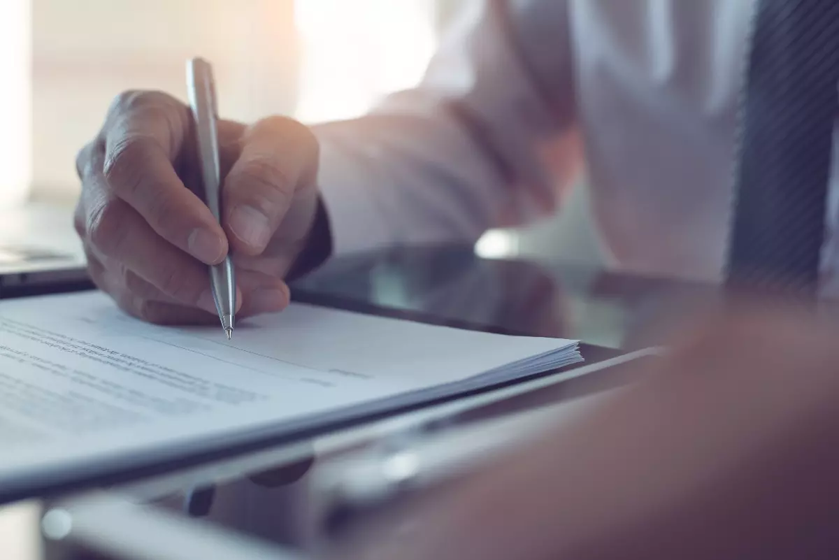 Hand holding pen and signing paperwork.