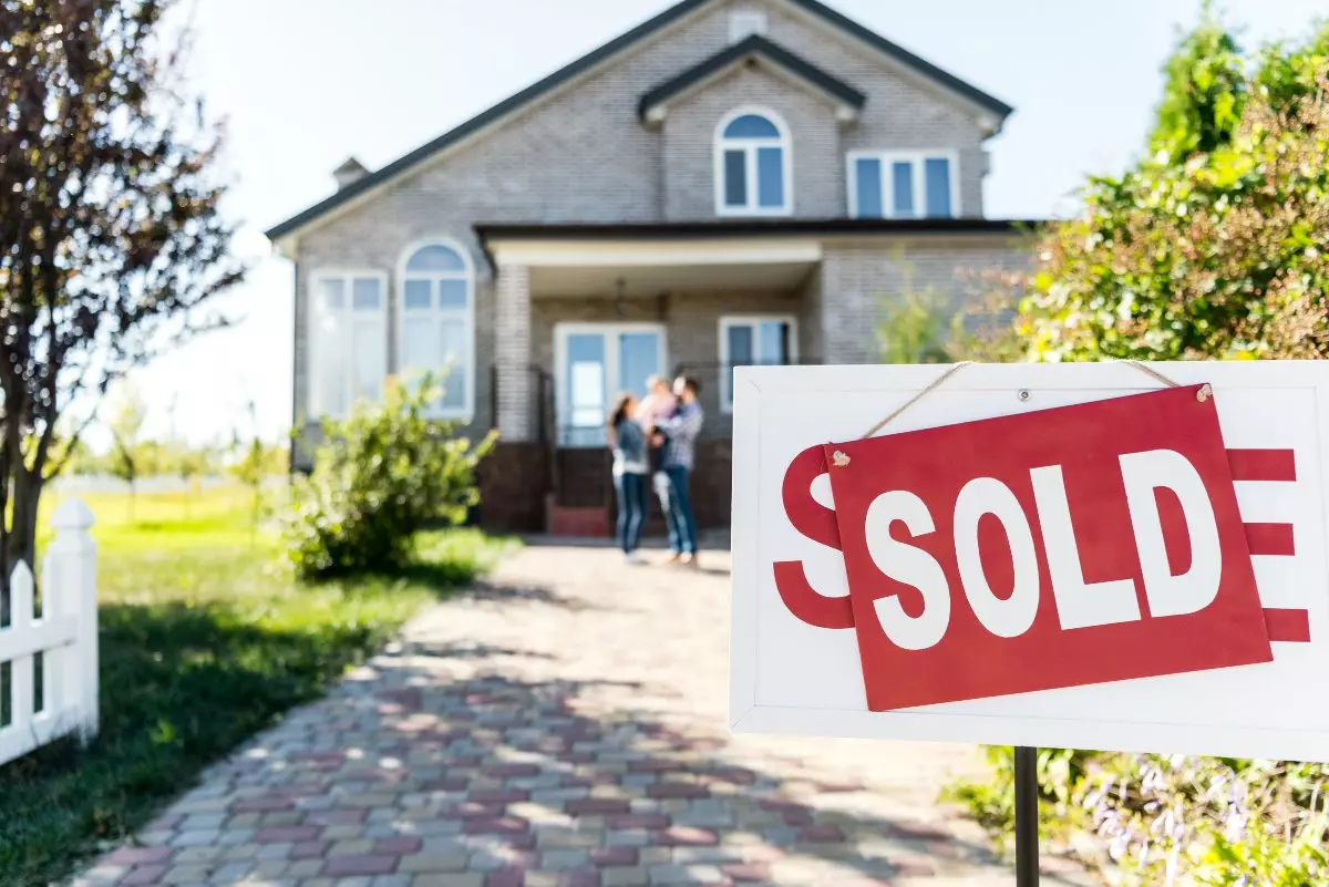 Family standing in front of house with a sold sign.