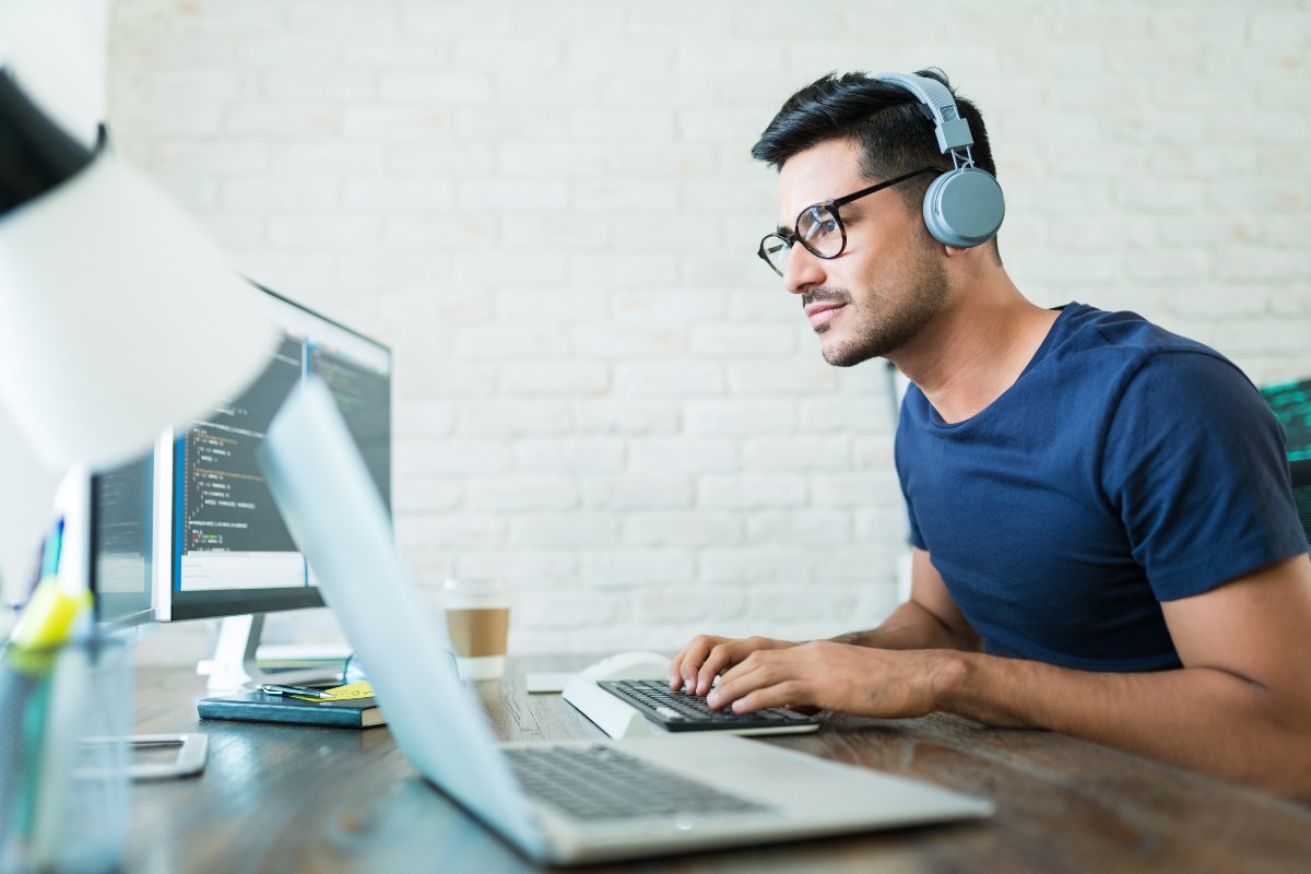 Young adult wearing headphones and transcribing on computer