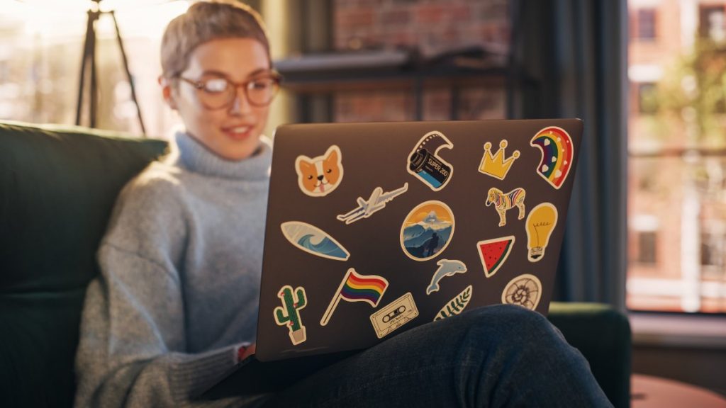 Young adult using laptop covered in stickers 