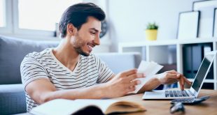 Smiling young adult paying bills on laptop