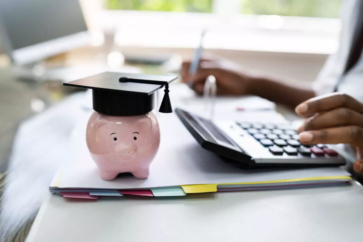 Individual using calculator next to a piggybank with a graduation cap